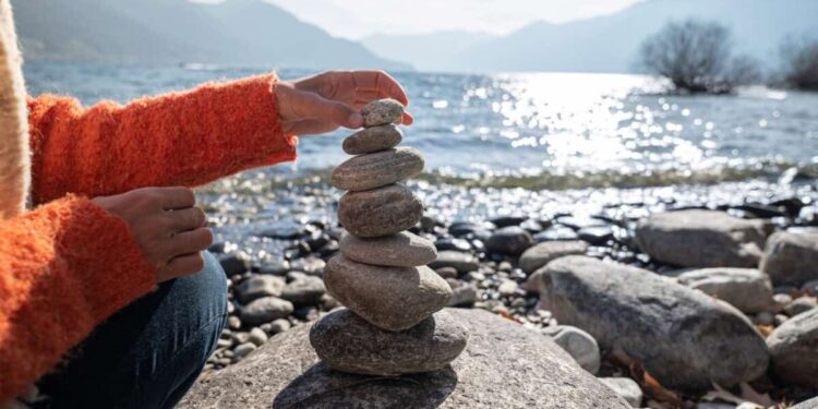 person stacking rocks by the lake