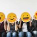 four people hold happy emoji masks