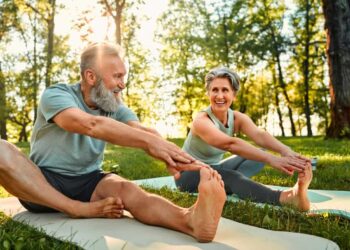 senior man and woman stretch their legs on yoga mats outside