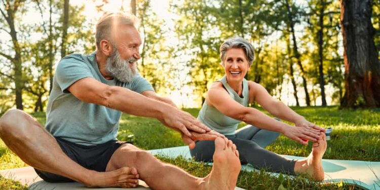 senior man and woman stretch their legs on yoga mats outside