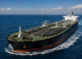 A large oil tanker carries rows of crude barrels across calm blue waters.