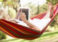 senior relaxes in hammock with e-book
