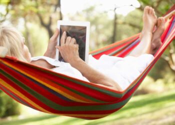 senior relaxes in hammock with e-book