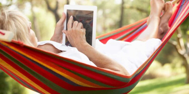 senior relaxes in hammock with e-book