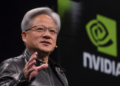 Jensen Huang speaks on stage beside a large Nvidia logo during a technology event.