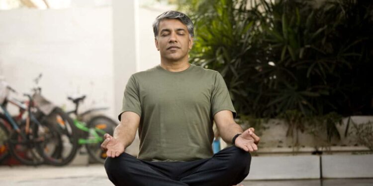 Man meditating in lotus position outdoor on patio