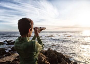 person with spyglass looks at ocean horizon