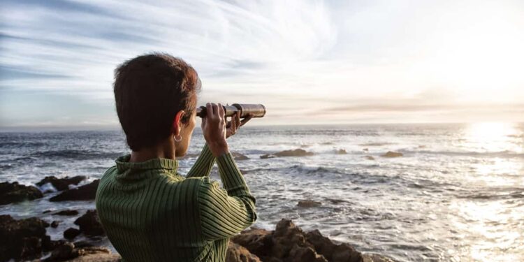 person with spyglass looks at ocean horizon
